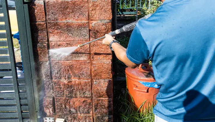 Pressure washing moss and grime off a brick pillar