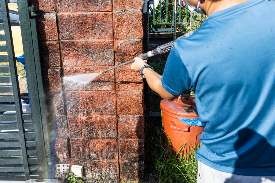 Pressure washing moss and grime off a brick pillar